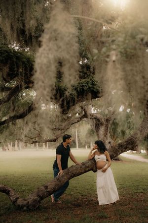 Couple sharing a tender moment by a large tree draped in Spanish moss during an outdoor maternity photo session.