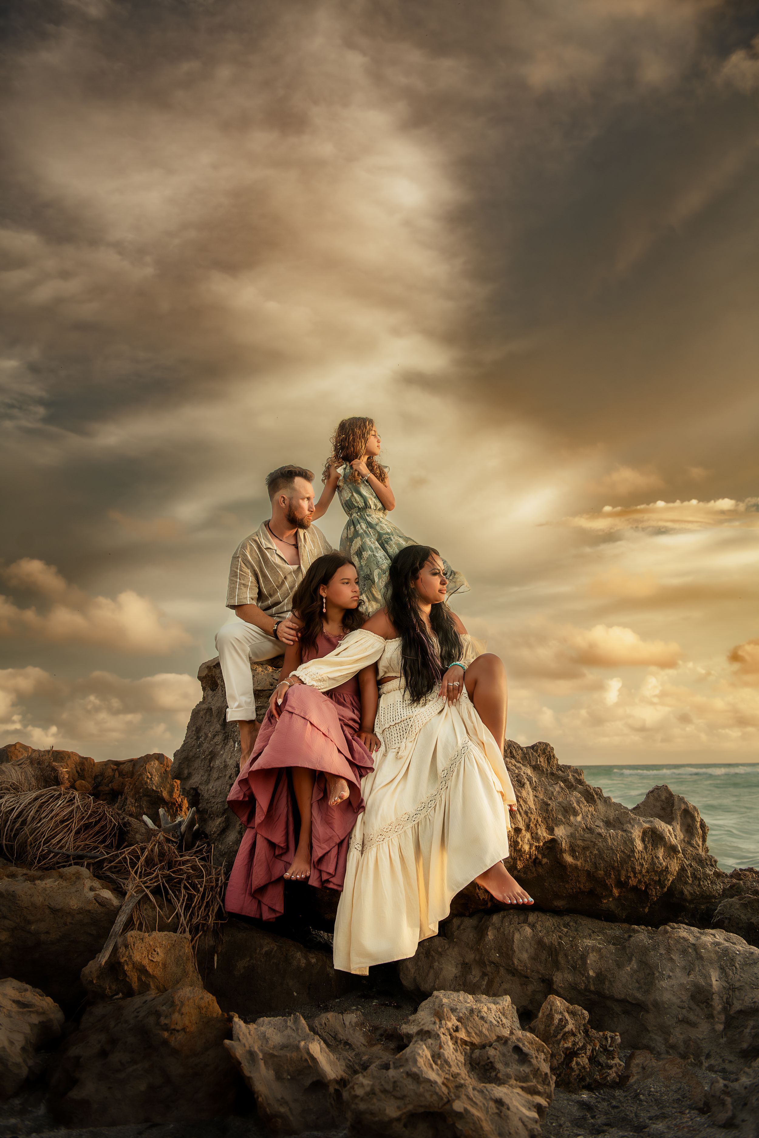 A group sits together on coastal rocks during sunset with dramatic golden clouds and ocean in the background.