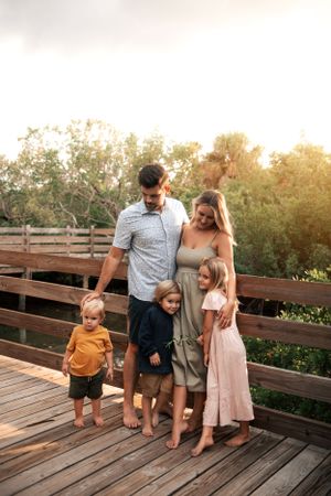 Family of five poses together on wooden deck during golden hour sunset.