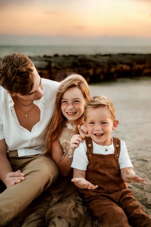 A family shares joyful laughter while sitting together on rocks at sunset by the water.