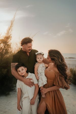 Family of four posing at sunset on a sandy beach, parents holding children in warm golden light.