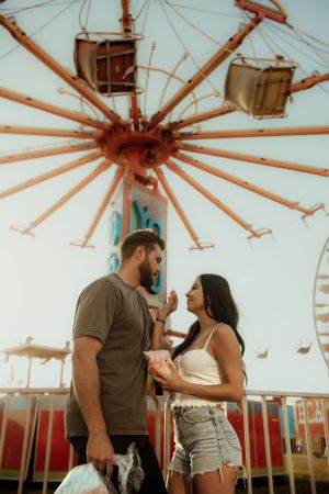 A couple shares a romantic moment underneath a spinning carnival ride at a fairground during golden hour.