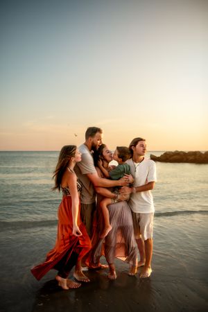 A group enjoys a peaceful sunset moment together on the beach with waves and rocks in the background.