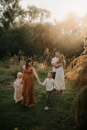 Family of four enjoying a golden hour outdoor photo session in a lush green field surrounded by trees.