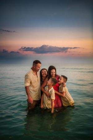 A family enjoying a warm sunset together while standing in calm ocean waters during golden hour.