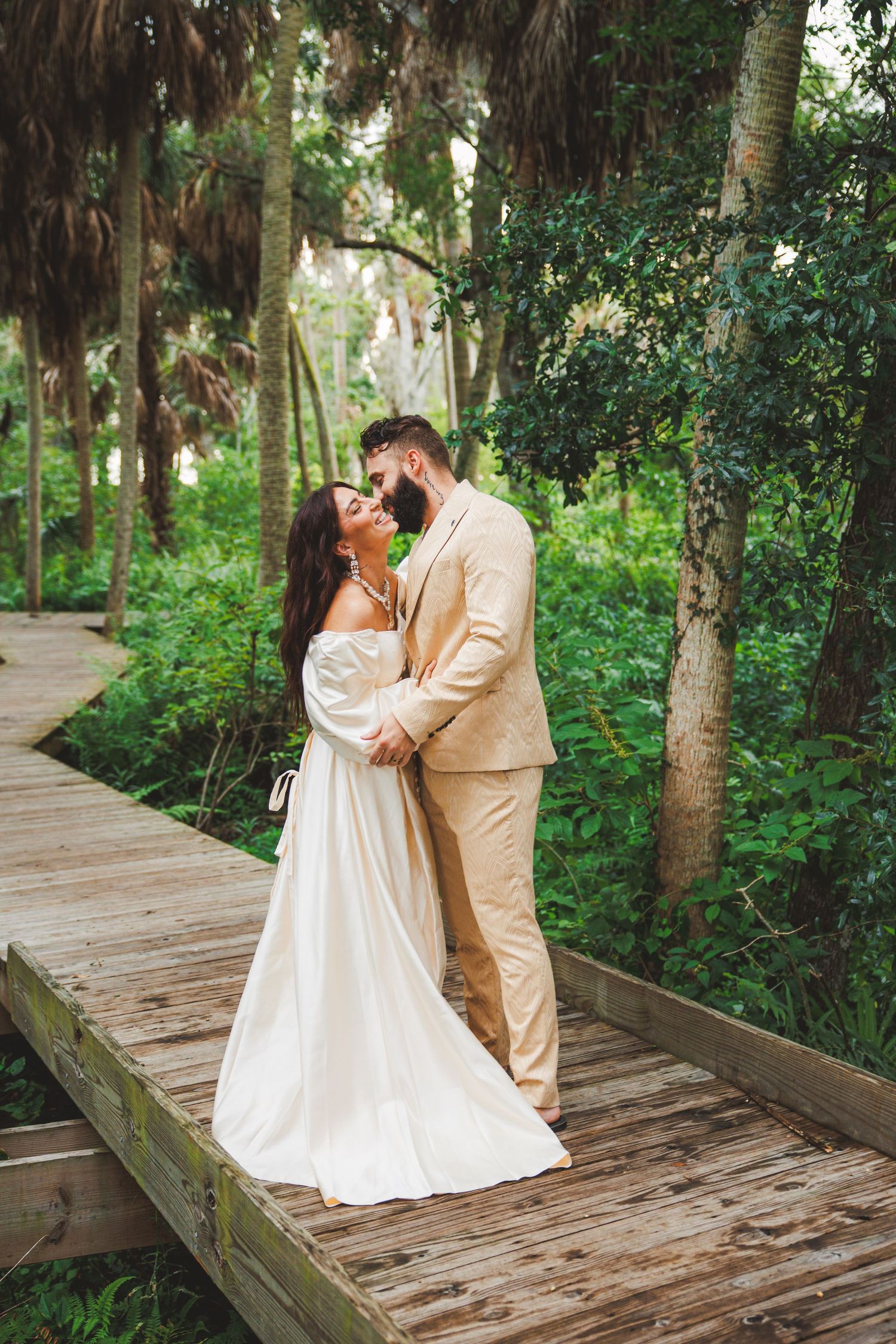 A romantic wedding portrait on a wooden boardwalk surrounded by lush forest scenery.