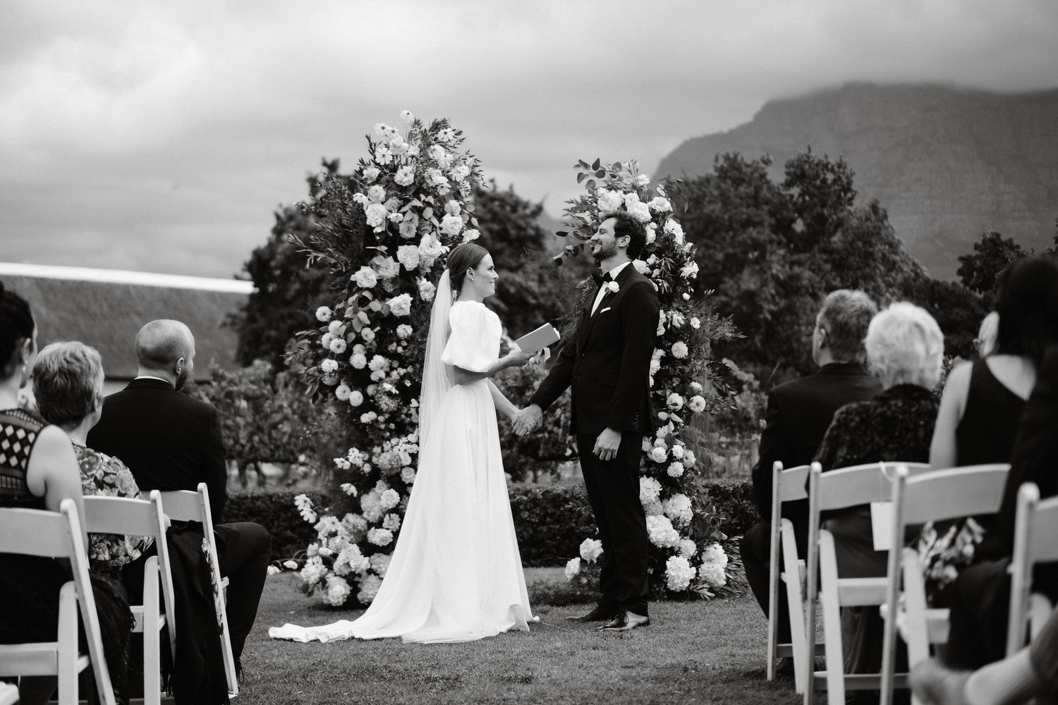 Wedding party stands on a dirt path surrounded by lush greenery and trees on an overcast day.