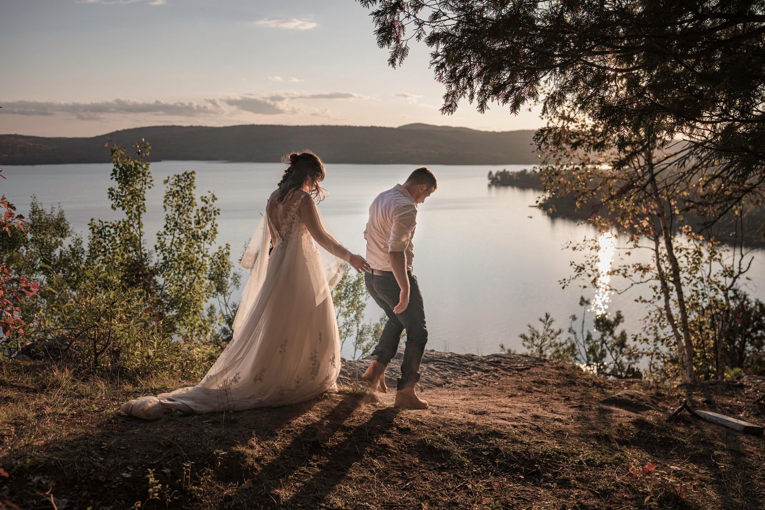 Eloping couple hike to the edge of a cliff. He guides her. Mountains in background., Mont Tremblant, Quebec, Canada.