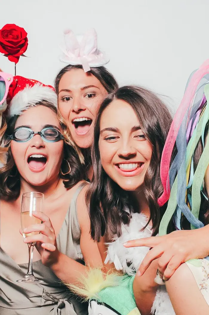Three excited party guests sharing laughs and champagne at a festive photo booth celebration.