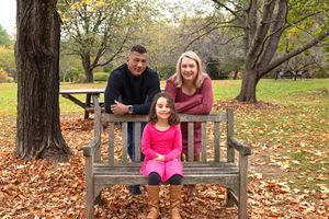 Family enjoying a fall day in the park surrounded by autumn leaves and wooden benches.