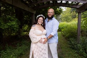 A couple poses under a wooden pergola in a garden setting, with the bride wearing a blush lace gown.