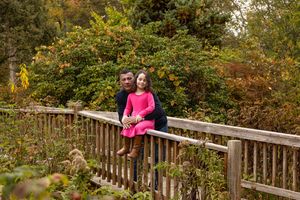 A couple stands on a wooden boardwalk surrounded by autumn foliage in a park setting.