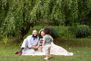 A couple enjoys a relaxing picnic date on a white blanket in a lush green park setting.
