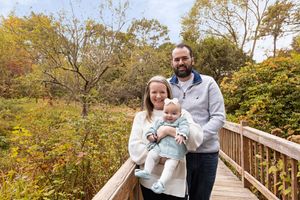 Family stands together on a wooden boardwalk surrounded by autumn foliage and trees on a sunny day.