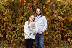 Family stands together in front of colorful fall leaves during outdoor portrait session.