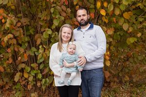 Family poses together against autumn foliage backdrop during outdoor photo session.