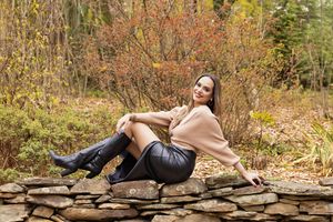 A person in autumn attire lies on a stone wall surrounded by colorful fall foliage in a forest setting.