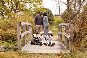 Romantic couple sits together on a wooden bridge surrounded by autumn foliage in a park setting.