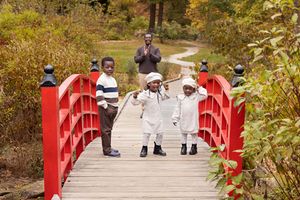 A series of photos showing people walking across a bright red wooden footbridge in an autumn garden setting.