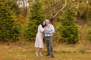 A couple shares a romantic embrace among evergreen trees and autumn foliage in a rustic outdoor setting.