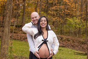 Happy couple poses together on wooden walkway surrounded by vibrant fall foliage in a forest setting.