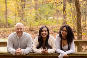 Group enjoys a casual moment together on wooden bench amidst fall forest scenery.