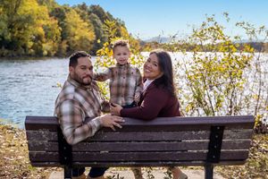 A couple sits together on a wooden bench overlooking a scenic autumn lake during a fall photo session.