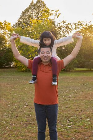 A joyful moment captured outdoors with a child riding on shoulders during golden hour in a park setting.