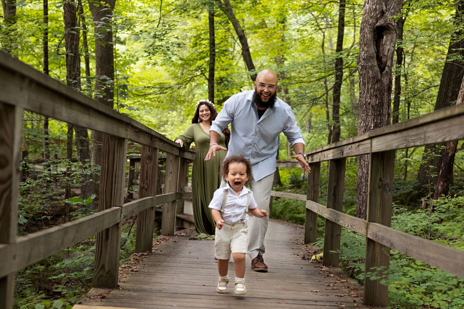 A wooden boardwalk trail winds through a lush green forest with people walking along the path.