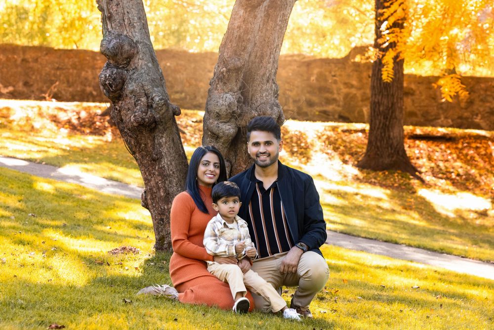 A family sits together on grass under autumn trees with golden sunlight filtering through the branches.