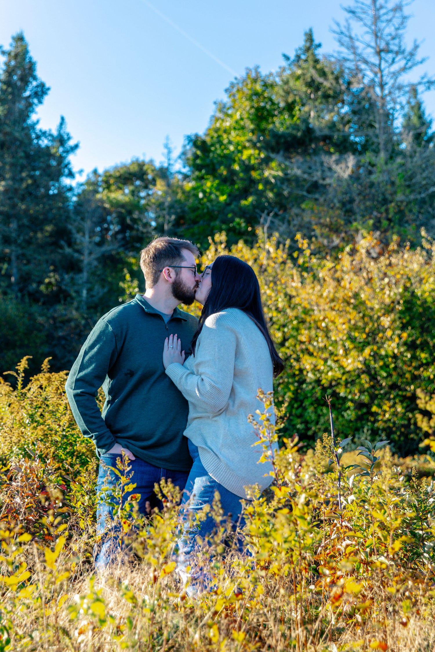 Couple sharing an intimate moment surrounded by autumn foliage and evergreen trees.
