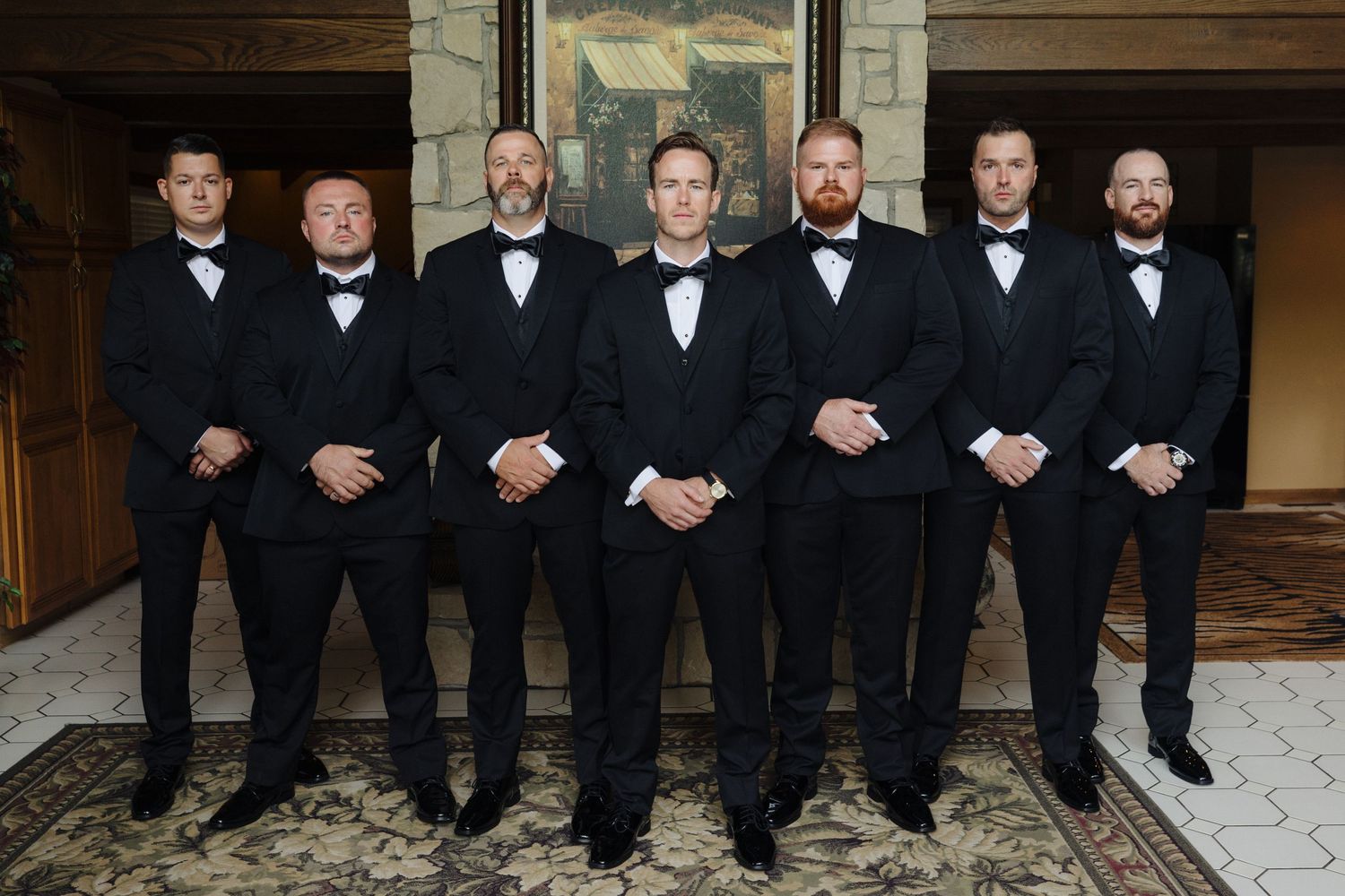 Groomsmen line up in classic black tuxedos and bow ties for formal wedding photo.