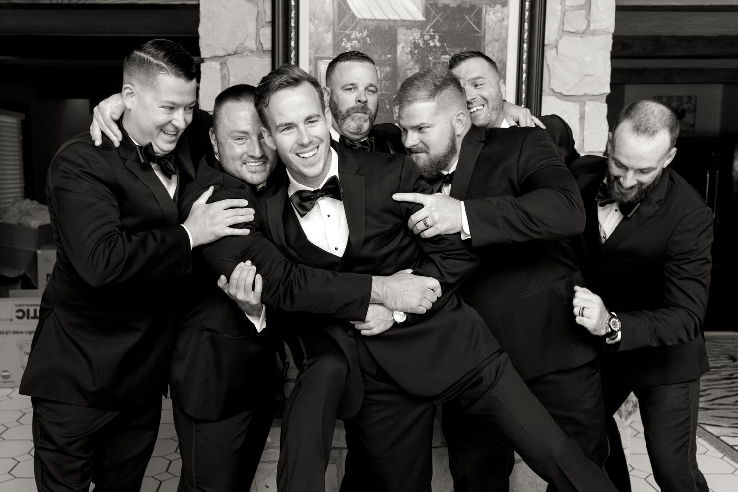 Groomsmen in black tuxedos pose playfully in a black and white group photo.