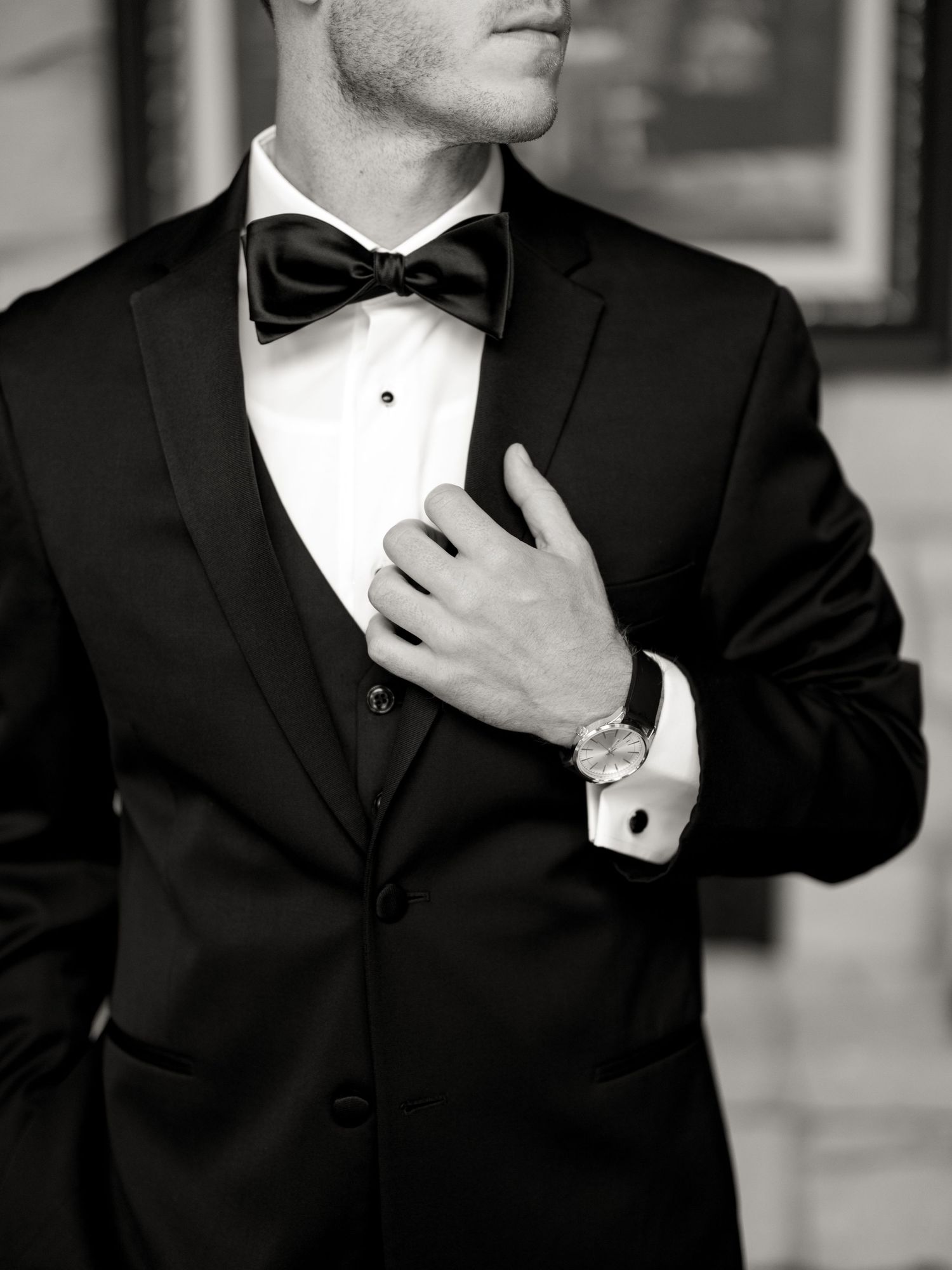 Close-up of a groom adjusting his black bow tie and tuxedo jacket.