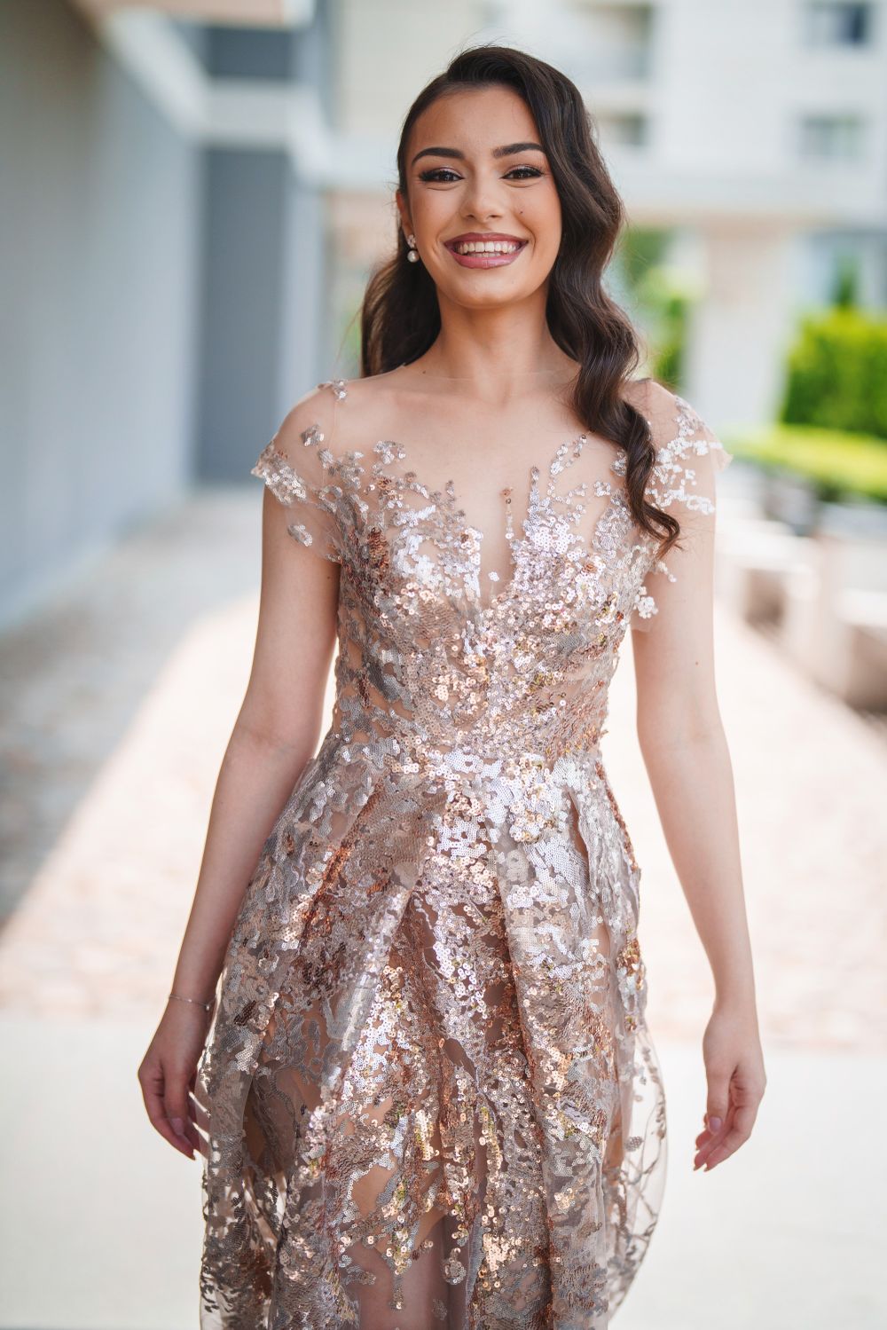 Stunning formal rose gold sequined dress with sheer details photographed in outdoor setting.