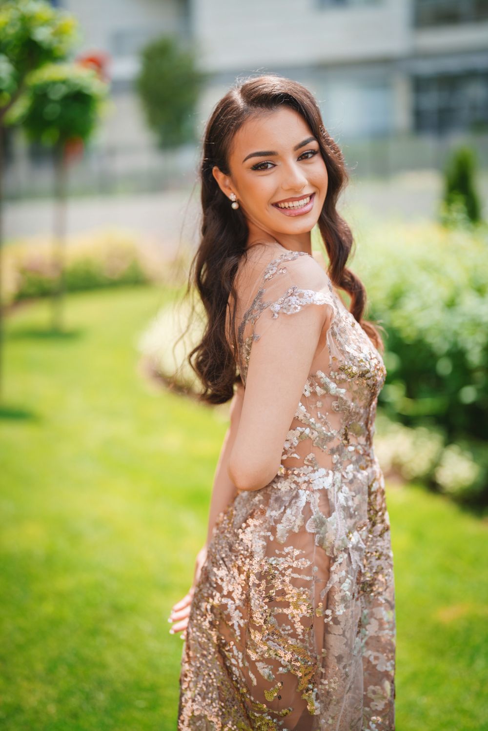 Side profile portrait in sparkling evening gown against lush garden background.