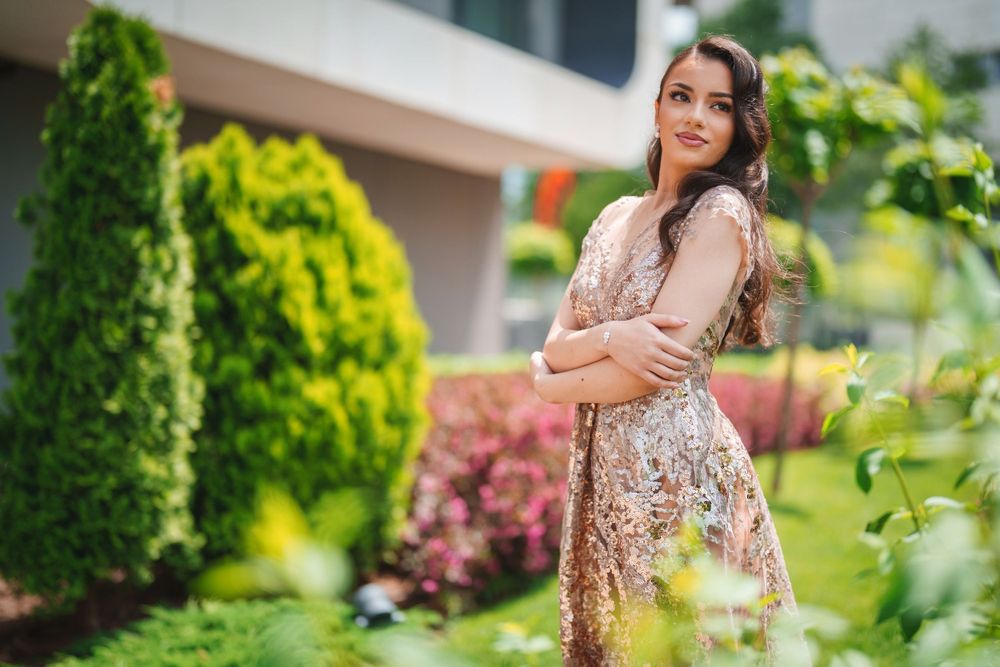 Romantic outdoor fashion portrait with sequined dress among manicured garden landscaping.