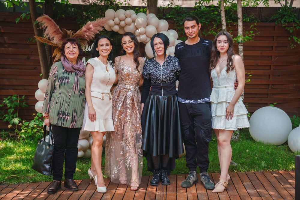 A group photo at a celebration with people wearing coordinated pastel and neutral outfits.