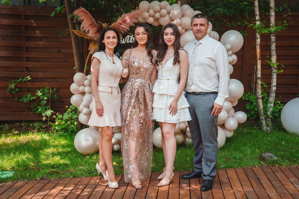 Four people pose together in front of a balloon arch and wooden wall at a celebration.