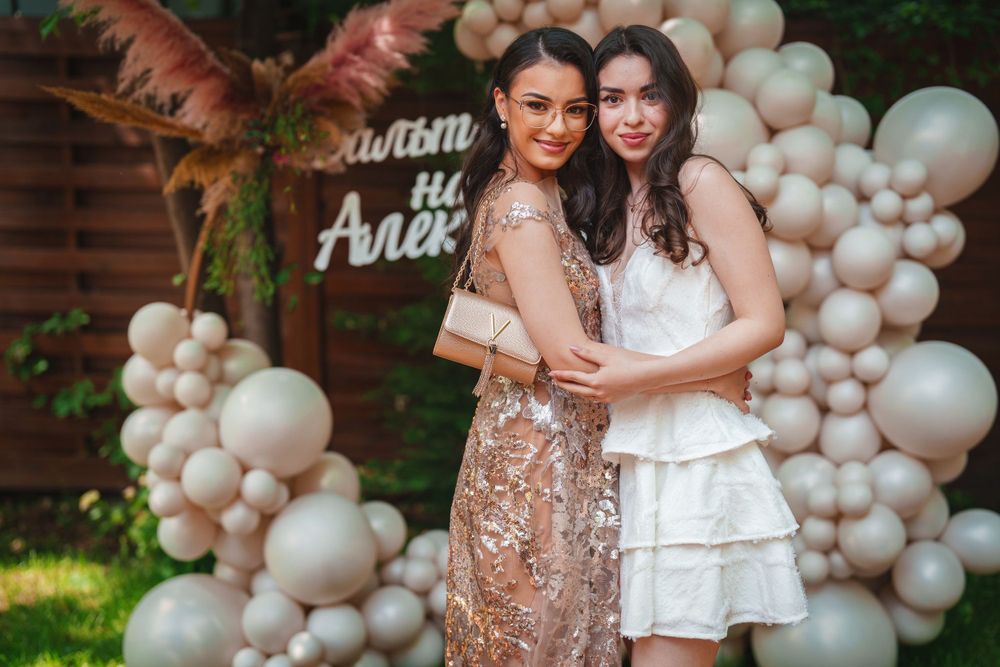Two people embrace while posing in front of a balloon arch and wooden wall.