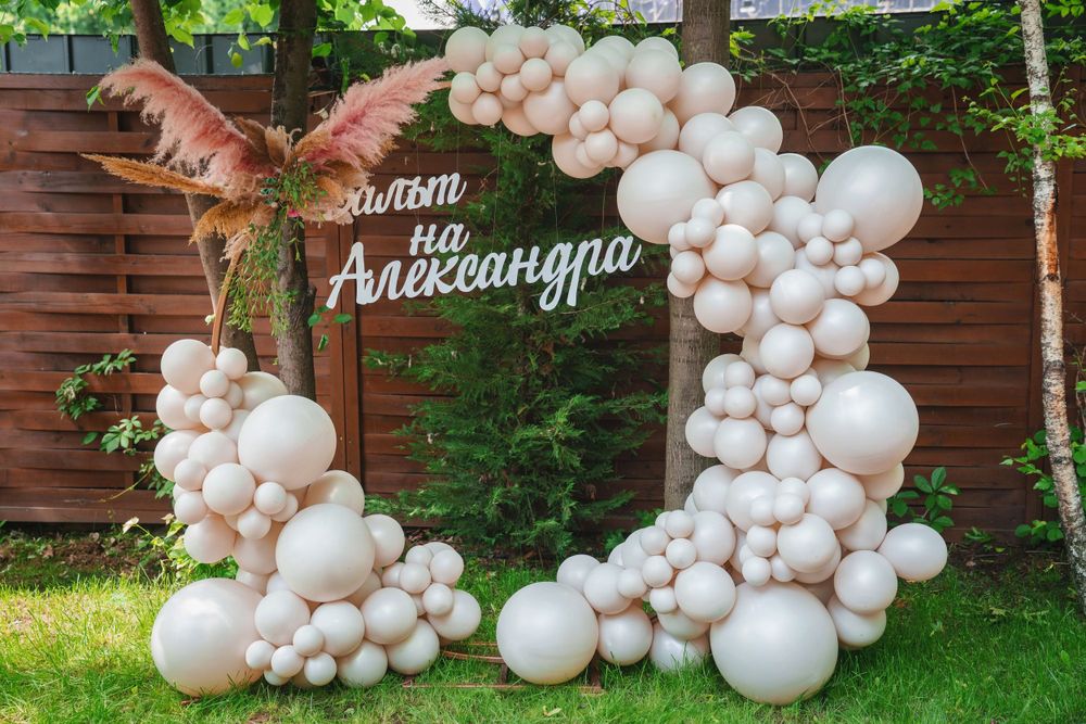 Elegant balloon arch with copper-colored feathers and white balloons against a wooden fence.