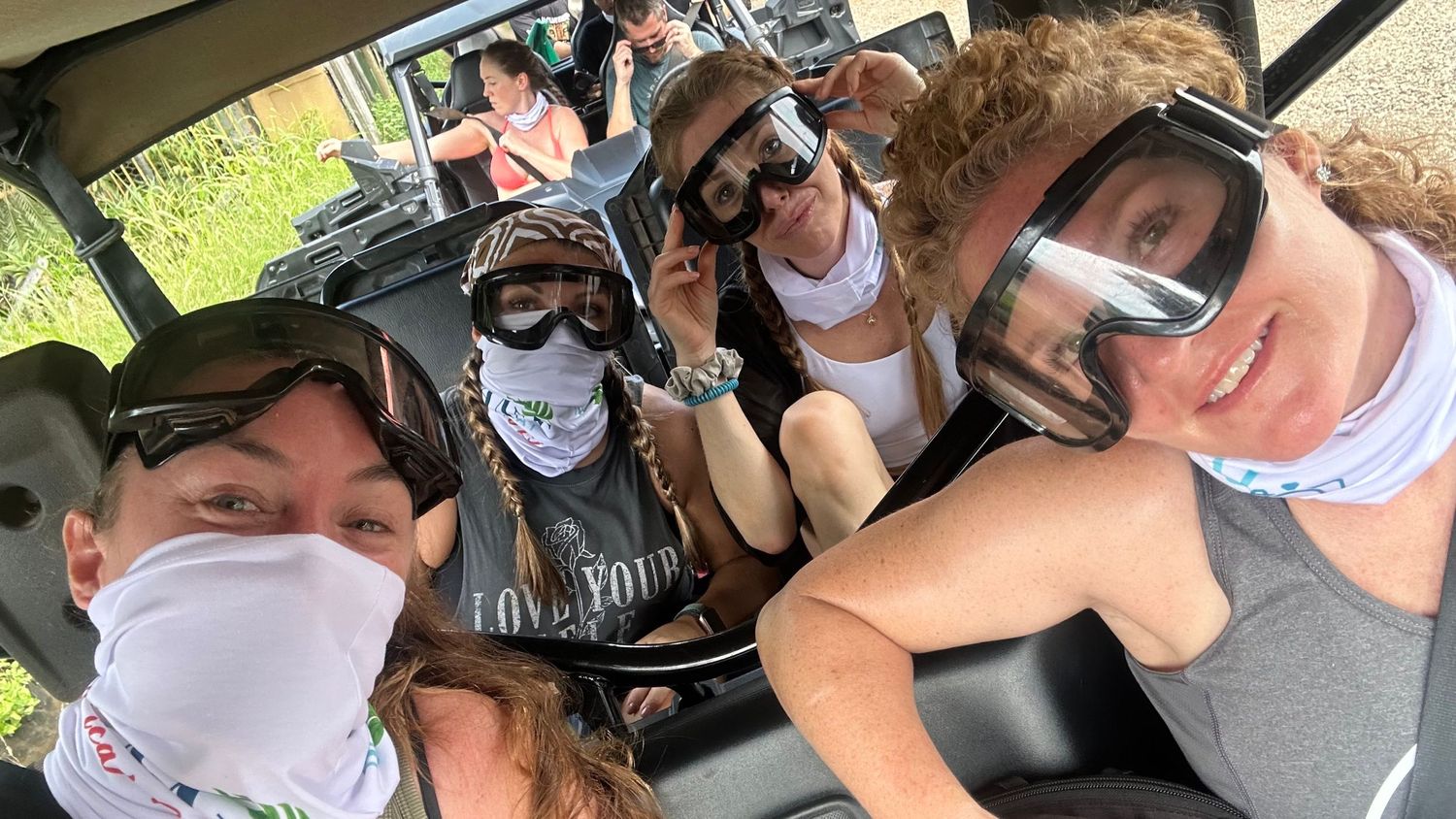 Group of people wearing protective face masks take a selfie together while sitting in a vehicle during outdoor activities.