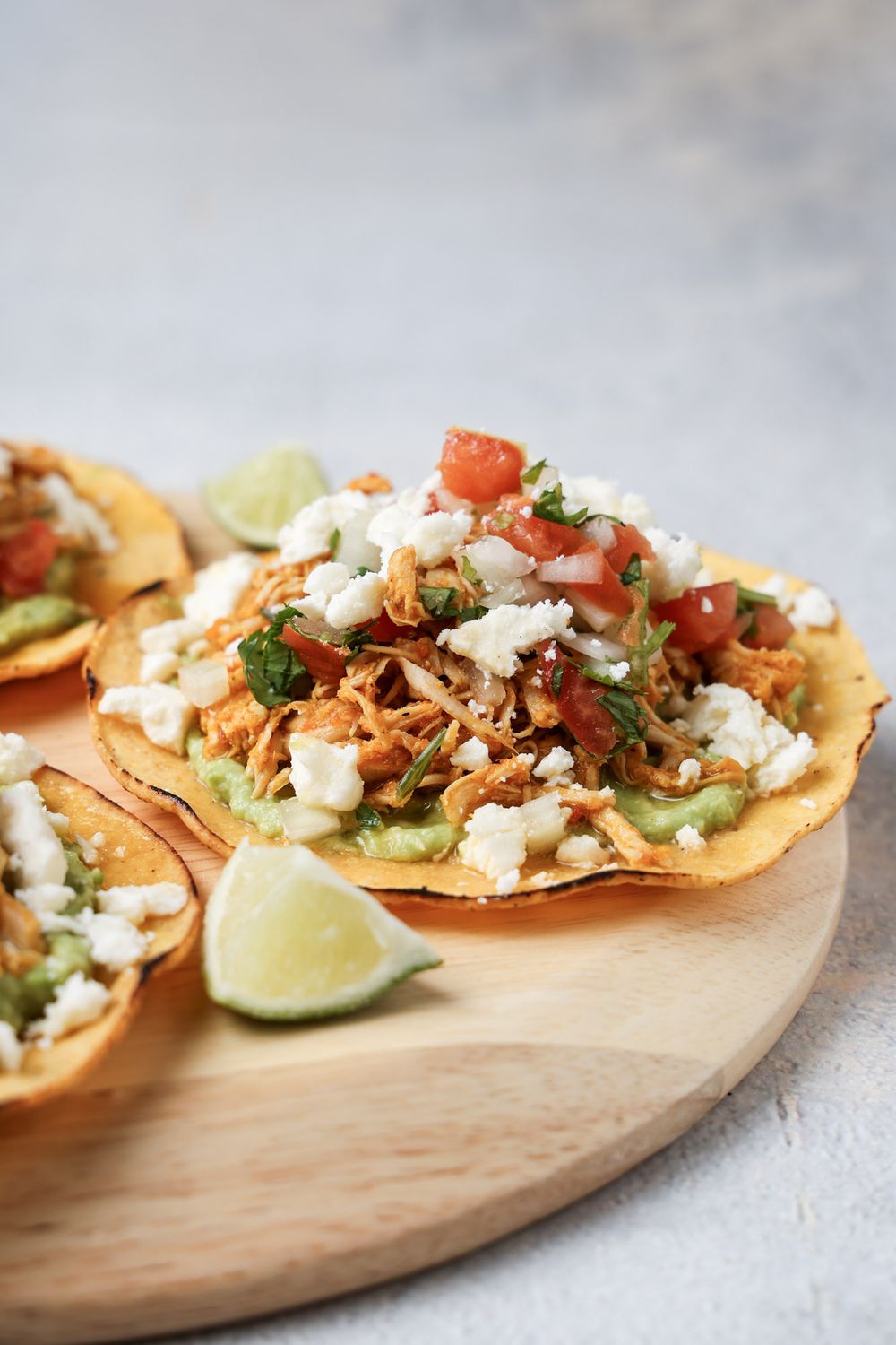 Mexican street tacos topped with shredded chicken, crumbled queso fresco, diced tomatoes and cilantro on a wooden board.