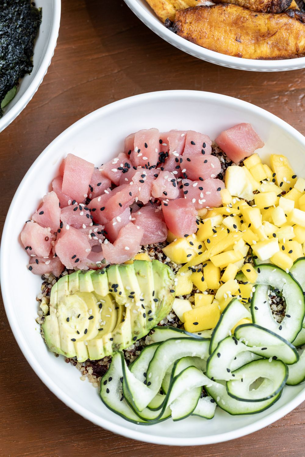 Fresh poke bowl with raw tuna, mango, avocado, cucumber and black sesame seeds served in a white bowl.