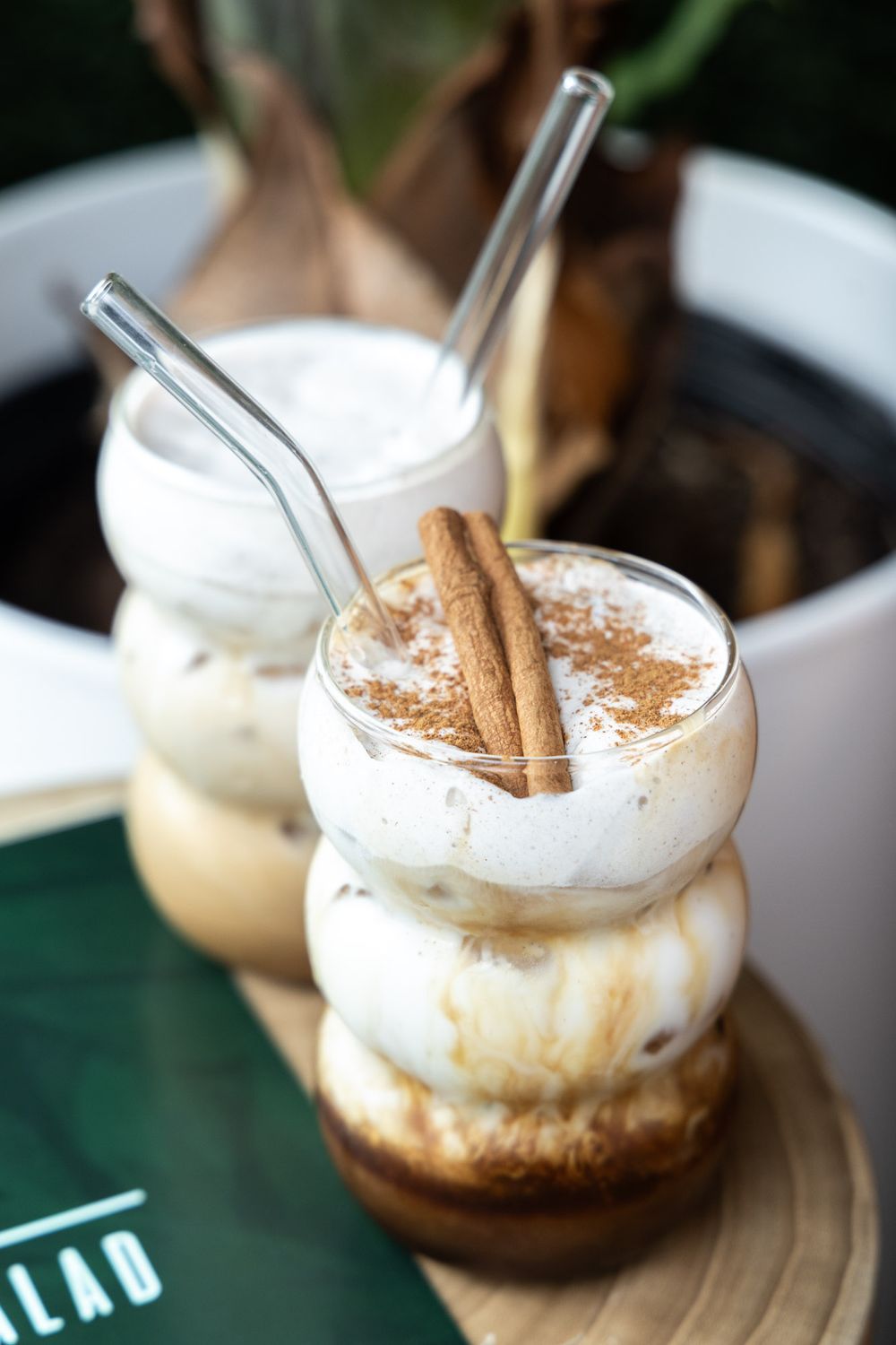 Creamy iced beverage topped with whipped cream and cinnamon sticks served in glass jars with metal straws.