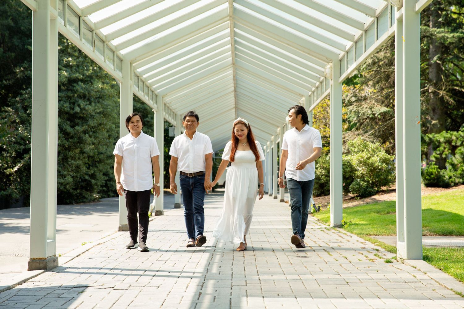 Group in white tops walks together under a bright covered walkway in a garden setting.