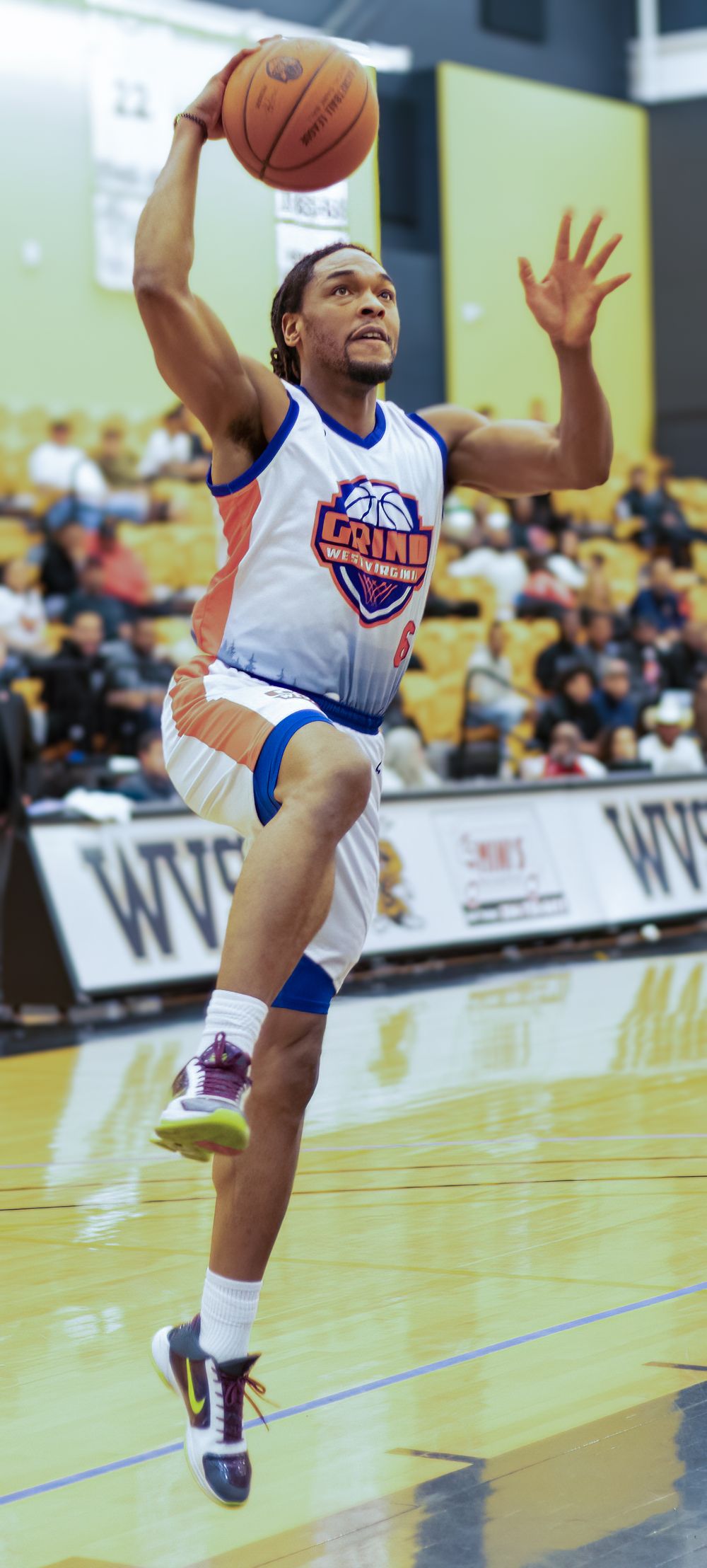 Basketball player in white and blue uniform leaps for layup during indoor game.