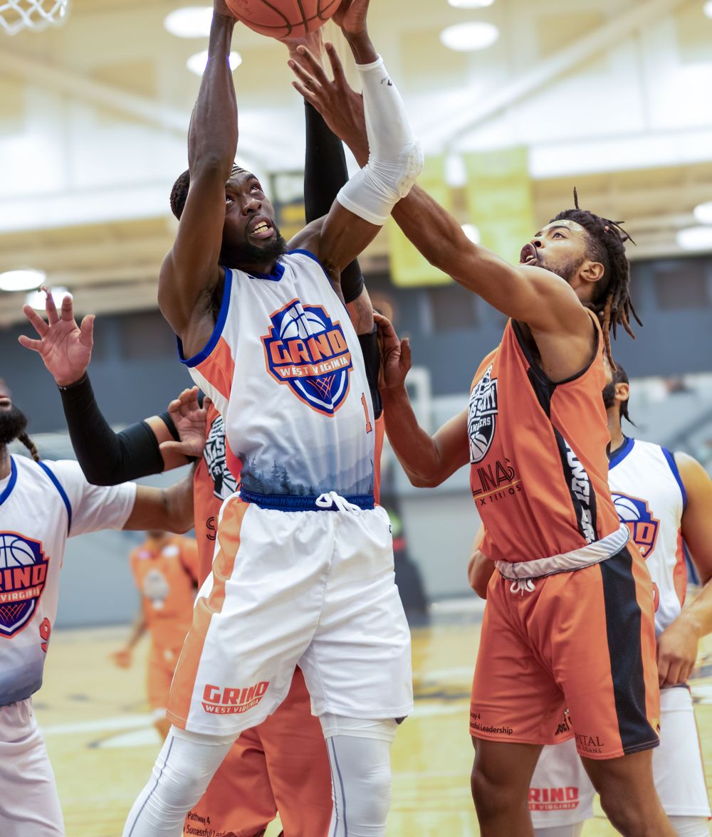 Basketball players compete for rebound during intense indoor game action.