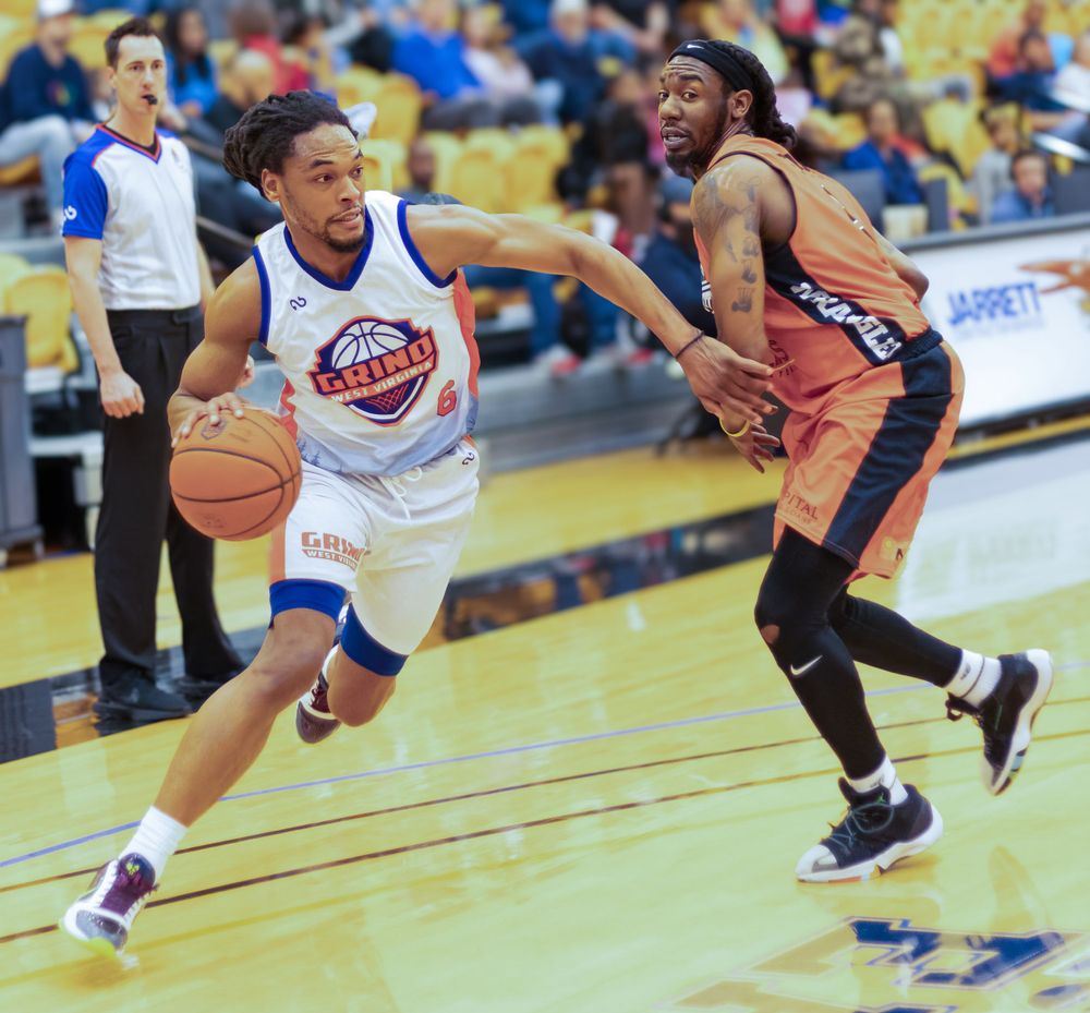 Basketball player dribbles past defender during competitive indoor game.