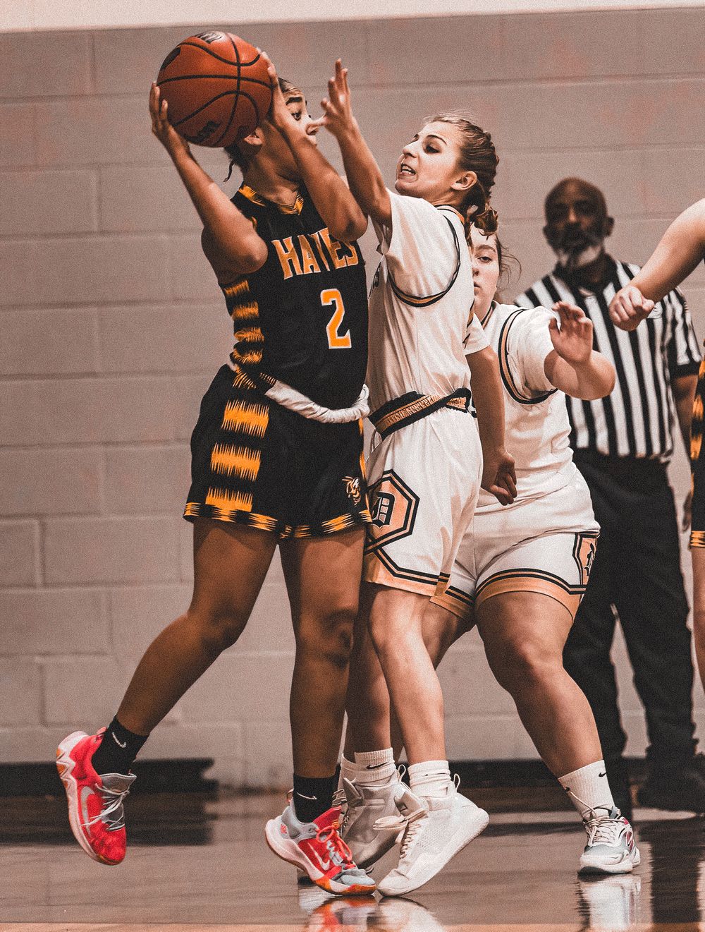 Players compete for possession during a basketball game between teams in white and black striped uniforms.